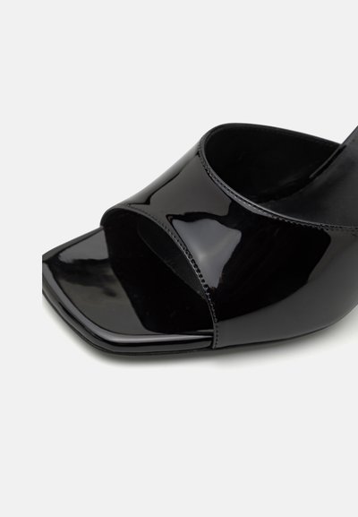 Black patent leather open-toe heeled shoe with a square toe and wide cross-straps, featuring a glossy finish and smooth texture.
