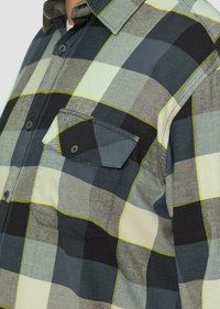 Flanellen shirt met een groot zwart, grijs en crème ruitpatroon met limoen groene accenten, knoopsluiting aan de voorkant en een borstzak.
