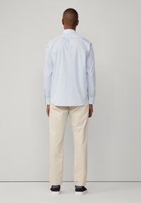 Lichtblauw overhemd met een rechte snit en lange mouwen, gecombineerd met beige broek en bruine sneakers met blauwe accenten.