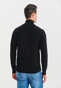 Czarny sweter typu golf z miękkiego materiału, z długimi rękawami. Tył charakteryzuje się gładką teksturą i dopasowanym krojem, zestawiony z niebieskimi dżinsami.