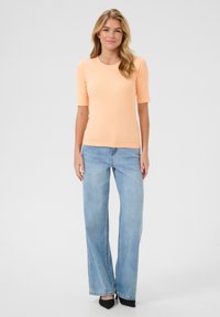 Peach ribbed short-sleeve top paired with light blue wide-leg jeans and black pointed-toe heels, standing against a neutral background.