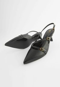 Melnas slingback augstpapēžu kurpes ar smailām purngalām, izgatavotas no gludas ādas. Iezīmē crisscross jostas ar zeltaini metāla detaļām.