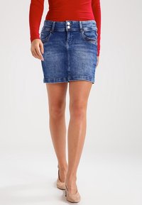 Džínová sukně s úzkým střihem, modrým odstínem, dvěma předními kapsami a viditelným zapínáním na knoflík v pase. Hladká textura, délka do půlky stehna.