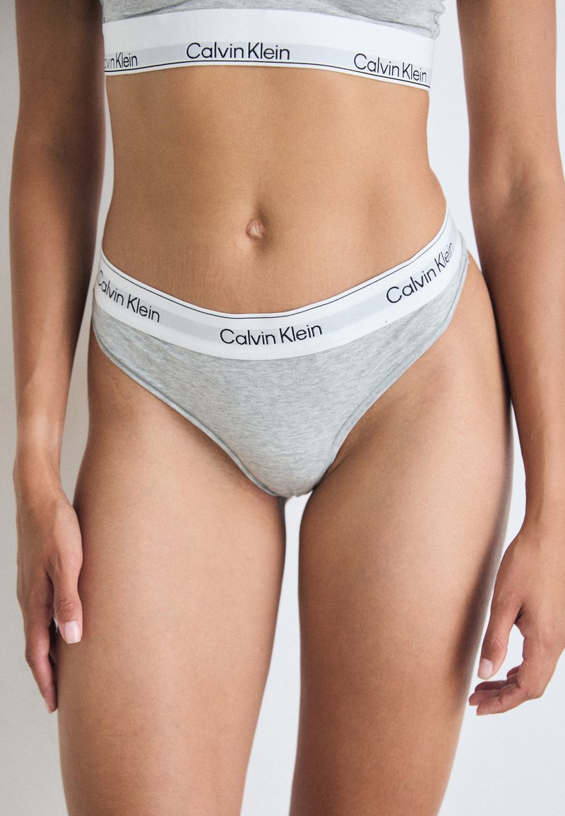 Culotte en coton gris avec une ceinture élastique blanche arborant le logo "Calvin Klein". Texture lisse, design ajusté, couverture minimale.
