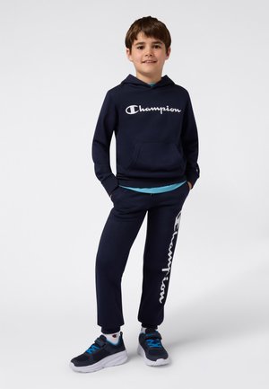 Sweat à capuche bleu marine avec le logo « Champion », pantalon de survêtement bleu marine assorti avec le logo sur la jambe, et chaussures bleu marine avec des accents bleus. Coupe athlétique.