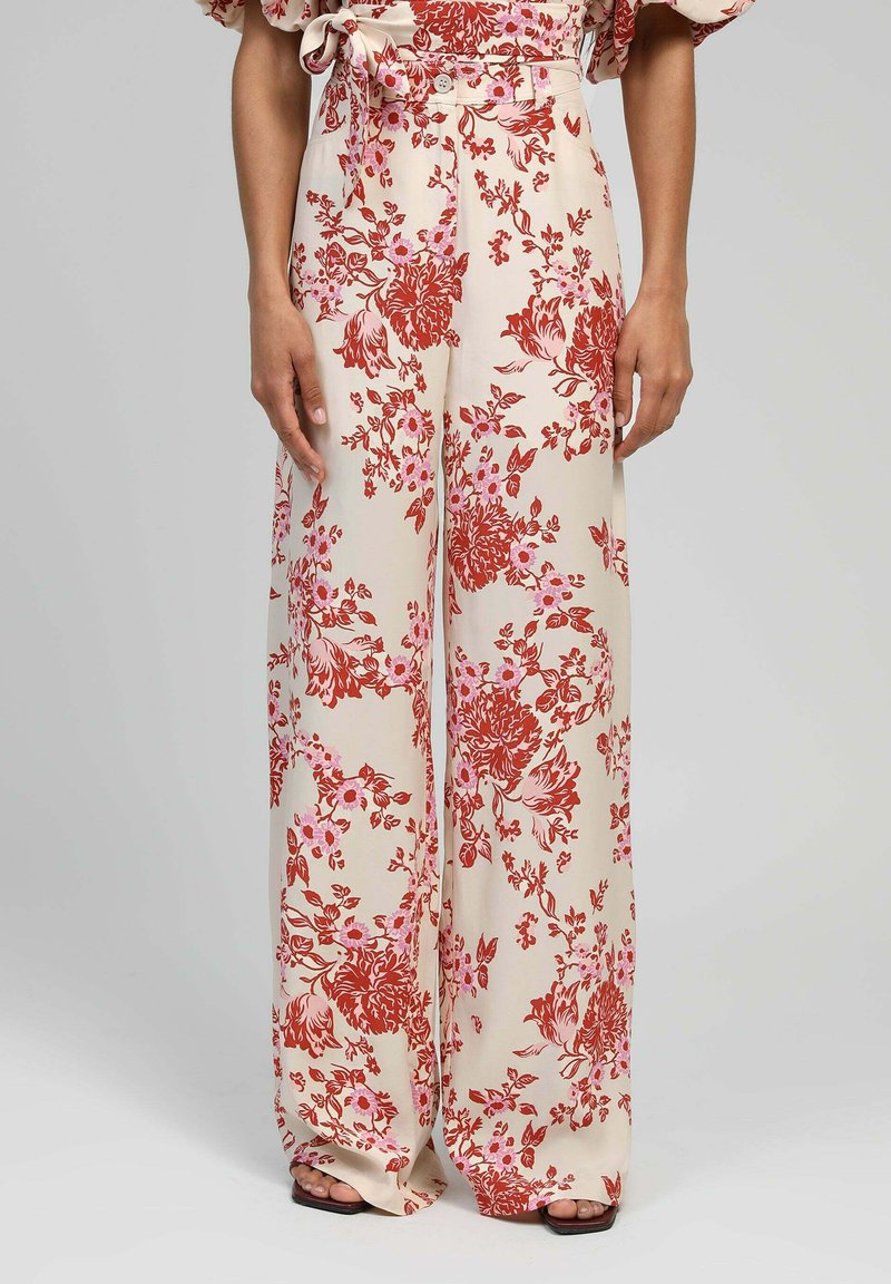 Pantalons large en tissu lisse, avec un fond crème orné de motifs floraux rouges et roses. Comprend un bouton avant et un détail de ceinture.
