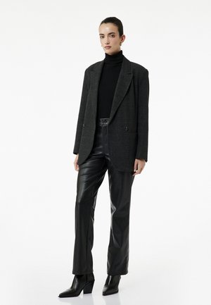 Grijze geruite oversized blazer met dubbele knopen, zwarte geribbelde coltrui, zwarte leren broeken en pointy block-heeled enkellaarsjes.