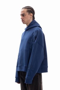 Niebieska bluza z kapturem wykonana z miękkiego materiału o luźnym kroju, z przeszyciami w kształcie krzyży na przodzie i rękawach. Posiada przednią kieszeń.