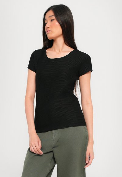 Black textured short-sleeve top with a rounded neckline. Paired with olive green pants, showcasing a relaxed fit and casual style.