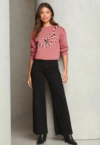 Sudadera rosa con diseño de caramelo en espiral y un acento de rosa, combinada con pantalones de pierna ancha negros y botas de tacón negras.