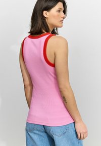 Roze geribbelde tanktop met een rode contrasterende halslijn. Kenmerkt zich door een aansluitende pasvorm, mouwloos ontwerp en gladde textuur.