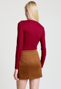 Rotes, eng anliegendes Langarmoberteil kombiniert mit einem braunen Wildleder-Minirock, der eine glatte Textur und ein schlichtes Design aufweist, von hinten betrachtet.