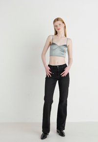Satenasto sivo kratko zgornje oblačilo z tankimi naramnicami, ki ima strukturirano zasnovo. Ujemajoče se s prilegajočimi črnimi jeans hlačami in koničastimi črnimi čevlji.