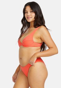 Conjunto de bikini de coral con costuras acanaladas que presenta un top de escote pronunciado con tirantes anchos y una parte inferior de cintura alta a juego. Textura suave y diseño minimalista.