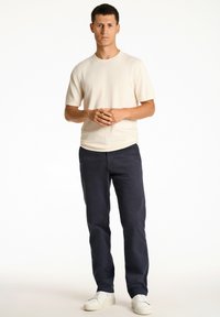 Beige ribbad kortärmad skjorta i kombination med marinblå byxor och vita sneakers, med en avslappnad passform och en enkel design.