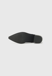 Black high-heeled shoe with a pointed toe and textured rubber sole. Features a sleek design and a contrasting light-colored heel accent.