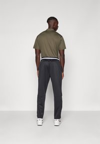 Olive green polo shirt paired with black athletic pants featuring a white waistband. The model faces away, showcasing a casual sporty look.