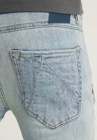 Ljusblå denimjeans med bakfickor som har ett distinkt triangulärt sömnadsmönster och en logotypkiet på midjan.