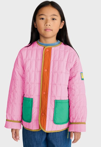 Jeune fille aux longs cheveux foncés portant une veste matelassée rose avec des poches vertes et un panneau avant orange boutonné.