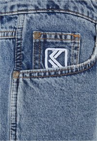 Džíny z denimu v svetlom modrom umývaní, s viditeľným prešívaním, malou náprsní kapsou s bielym výšivkovým logom a detailom z kovového gombíka.
