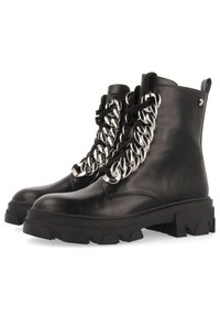Botas de tobillo de cuero negro con suela gruesa, que presentan acentos de cadenas de plata sobredimensionadas en la parte frontal. Cordones de tela y un lazo trasero para facilitar el calzado.