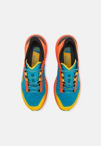 Des chaussures de sport avec un dessus en maille turquoise, des accents orange, une semelle jaune et une doublure intérieure noire avec une surface texturée et des lacets.