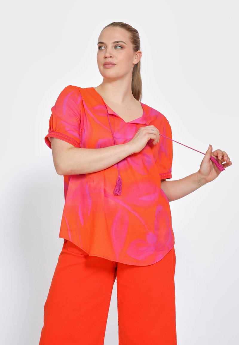 Heldere oranje blouse met roze bloemenpatronen, korte pofmouwen en een v-halslijn, met een strikkoord en een kwastdetail.