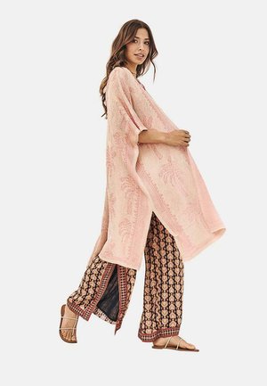 Túnica de kimono texturizada en color rosa con un patrón de hojas de palma, combinada con pantalones de pierna ancha impresos en negro con acentos florales rojos y sandalias planas marrones.