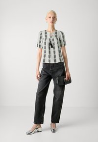 Blusa azul claro con patrón de hojas negras, mangas cortas abullonadas y detalle de lazo en el cuello. Jeans negros de cintura alta y zapatos de tacón bloque metálicos.