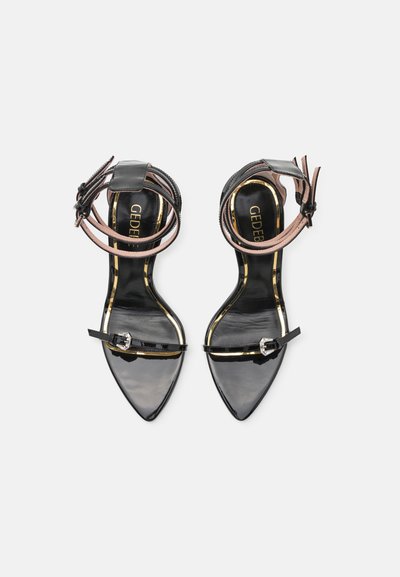 Sandalias de tacón alto de charol negro con punta afilada. Cuentan con una delgada correa en el tobillo y un acento de hebilla decorativa.