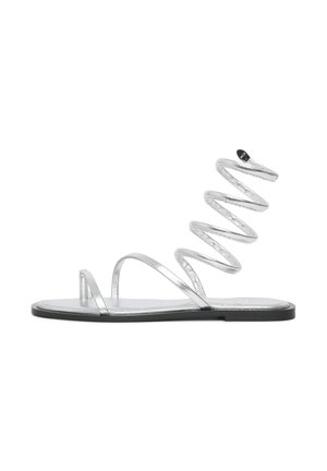Sandales argentées à semelle plate, dotées de fines lanières et d'un design en spirale. Le matériau a une finition métallique avec une texture lisse.