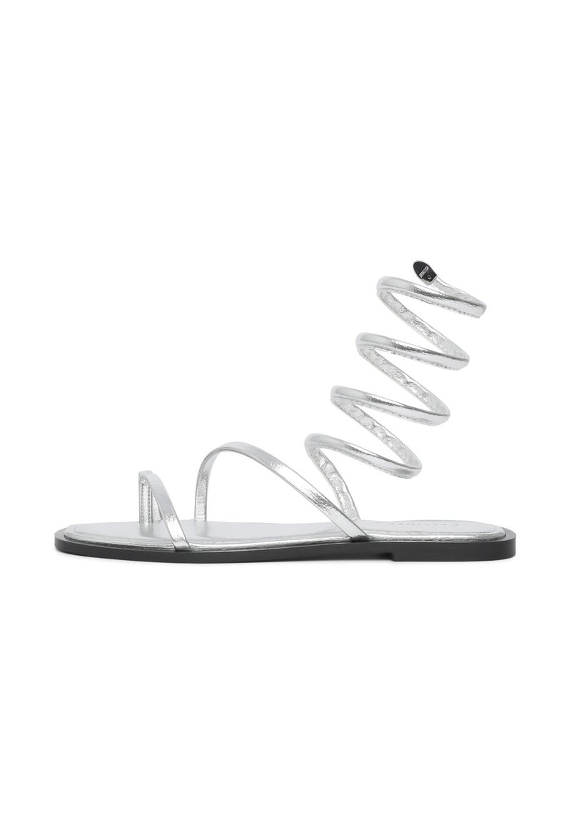 Silberne Sandalen mit flacher Sohle, die dünne Riemen und ein spiralförmiges Design aufweisen. Das Material hat ein metallisches Finish mit einer glatten Textur.