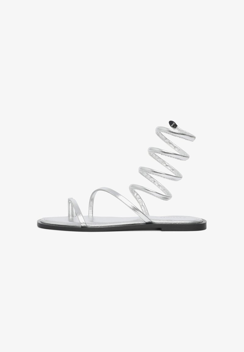 Sandales argentées à semelle plate, dotées de fines lanières et d'un design en spirale. Le matériau a une finition métallique avec une texture lisse.