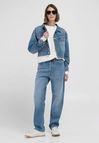 Ljusblå denimjacka med knappstängning, kombinerad med en vit sweatshirt och ljusblå löst sittande jeans. Vita sneakers fulländar looken.