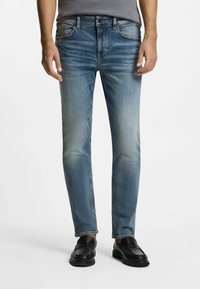 Jeans de mezclilla azul claro con corte recto, que presentan un deslavado sutil, diseño de cinco bolsillos y costuras en contraste, combinados con mocasines negros.