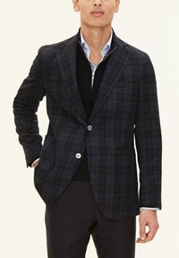 Marinblå rutigt blazer med strukturfinish, två knappar och uppvikta slag. Bärs över en svart tröja och en ljusblå skjorta med krage.