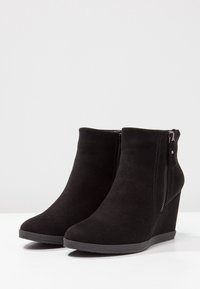 Bottines chevillières en suède noir avec fermeture éclair sur le côté, orteils ronds et semelles en caoutchouc texturé. Présente un design élégant et une finition mate.