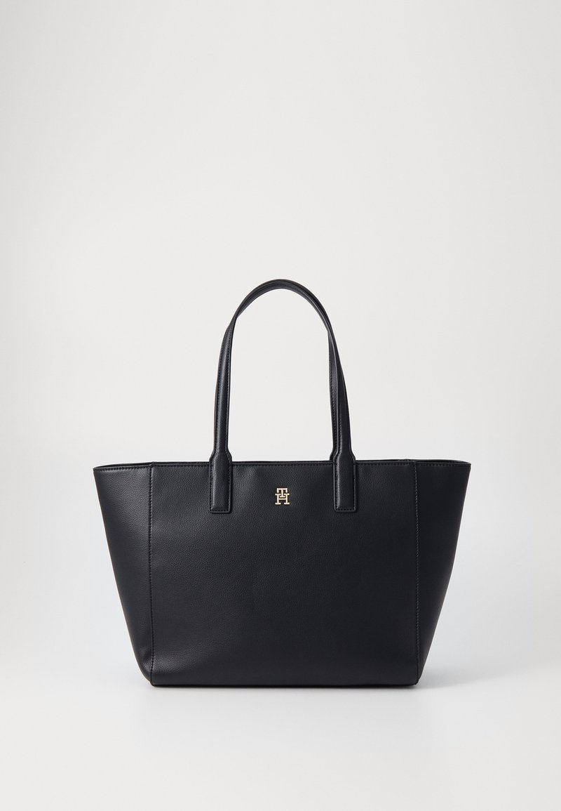 Zwarte leren tote bag met een gestructureerd ontwerp, twee lange handvatten en een metallic logoaccent aan de voorkant. Gladde textuur, minimalistische stijl.