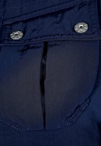 Navy blue fabric with a smooth texture, featuring a pocket with a flap closure, metallic snaps, and stitching details.