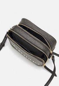 Borsa a tracolla nera in pelle con doppie tasche con zip; presenta dettagli in oro, materiale testurizzato e un logo bianco ben visibile.