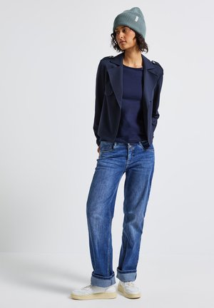 Navy blazer with a structured design, navy shirt, and blue jeans. The outfit features a knit grey beanie and white sneakers.