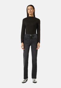 Schwarzes Langarmoberteil kombiniert mit dunklen Denim-Jeans. Die Jeans haben eine taillierte Passform und gerade Beine, mit einem dezenten Waschungseffekt und minimalen Nähten.