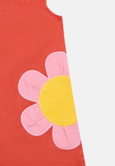 Tela roja con una gran aplicación de una flor de pétalos rosas con un centro amarillo en la parte inferior derecha.