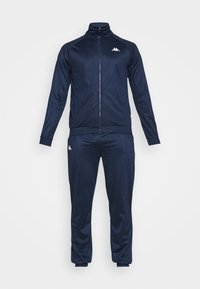 Ensemble de survêtement bleu marine deux pièces avec une veste zippée et un pantalon assorti, avec des logos Kappa blancs sur la poitrine et la cuisse.