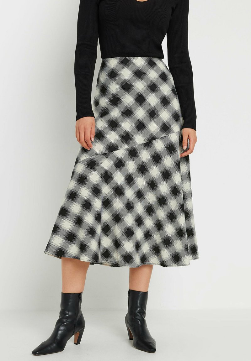 Jupe midi à carreaux noir et blanc avec un ourlet évasé, en tissu lisse et design taille haute, assortie à des bottines noires.