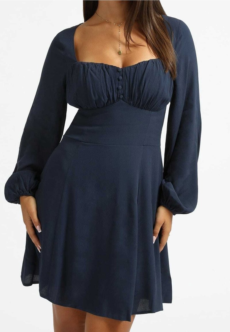 Granatowa sukienka z usztywnionym korpusem, bufiastymi długimi rękawami i rozszerzanym dołem. Posiada materiałowe guziki i teksturowane wykończenie.