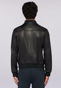 Chaqueta de cuero negro con un cuello y puños acanalados, que presenta una textura suave, un diseño sencillo y detalles en las costuras en la parte posterior.