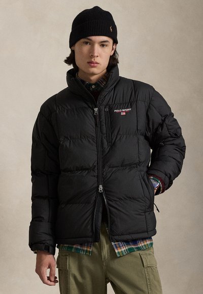Chaqueta acolchada negra con diseño acolchado, cremallera frontal y logo "POLO SPORT". Se lleva sobre una camisa de cuadros y combinada con pantalones cargo oliva.