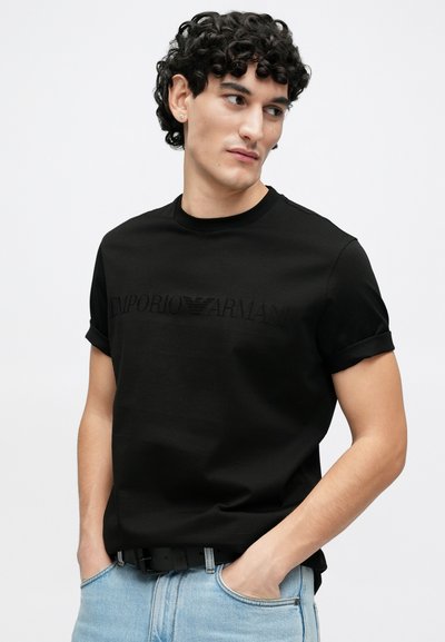 Μαύρο βαμβακερό T-shirt με στρογγυλή λαιμόκοψη, κοντά γυρισμένα μανίκια και τονικό λογότυπο "EMPORIO ARMANI" στο στήθος.