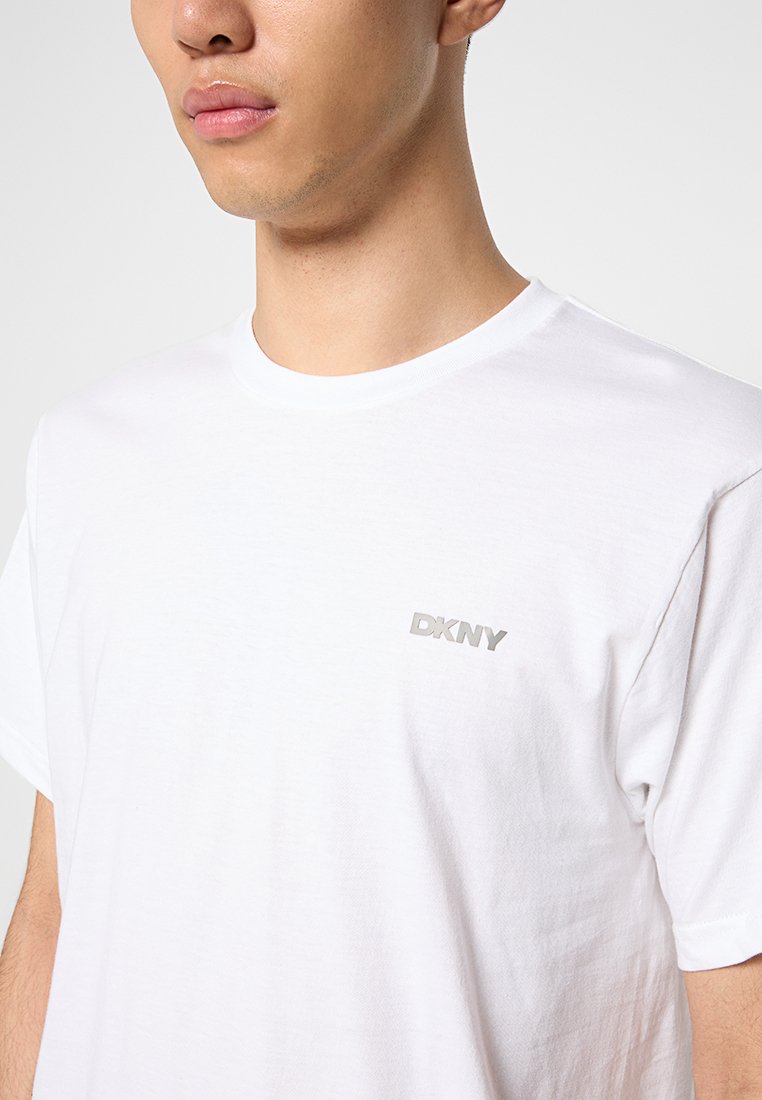 Biała bawełniana koszulka z okrągłym dekoltem i krótkimi rękawami. Zawiera małe, srebrne logo DKNY po lewej stronie klatki piersiowej.